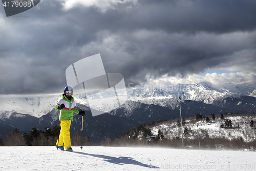 Image of Young skier with ski poles in sun mountains and cloudy gray sky 