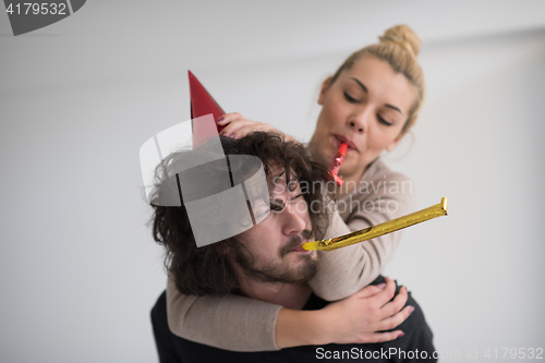 Image of couple in party hats blowing in whistle