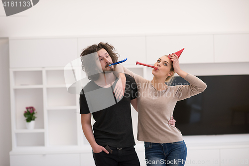 Image of couple in party hats blowing in whistle