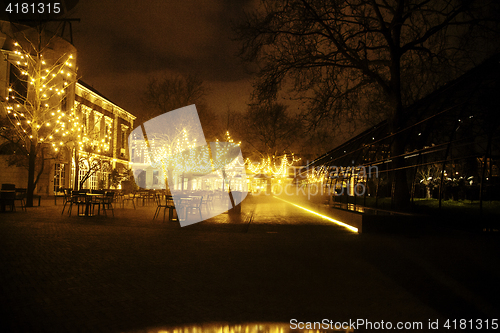 Image of empty night restaurant, lot of tables and chairs with noone, magic fairy lights on trees like christmas celebration