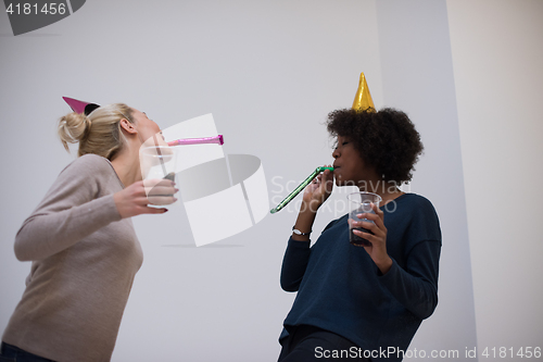 Image of smiling women in party caps blowing to whistles