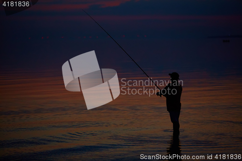 Image of Silhouette of fishermen on quiet ocean with rays sunset