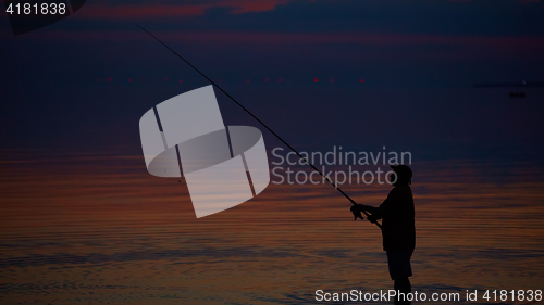 Image of Silhouette of fishermen on quiet ocean with rays sunset