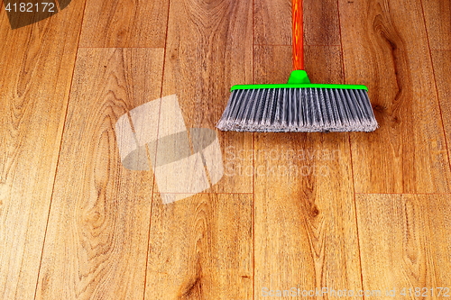 Image of cleaning wooden floor with green plastic broom
