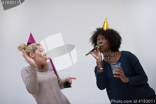 Image of smiling women in party caps blowing to whistles