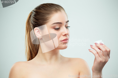 Image of Portrait of young beautiful woman applying moisturizing cream on her face