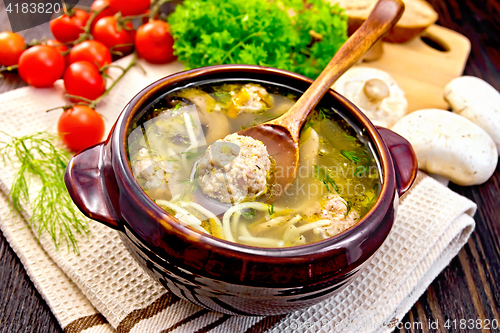 Image of Soup with meatballs and spoon in clay bowl on board