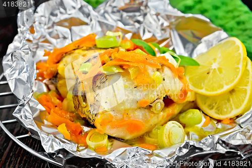 Image of Pike with carrots and lemon in foil on dark board
