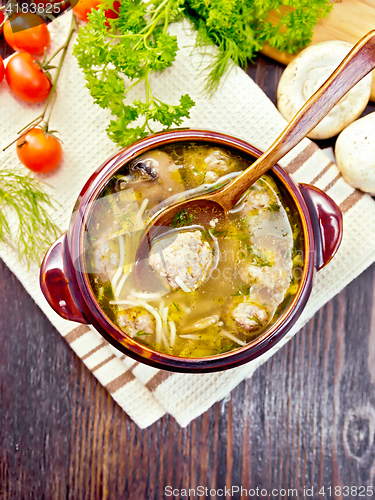 Image of Soup with meatballs and spoon in clay bowl on board top