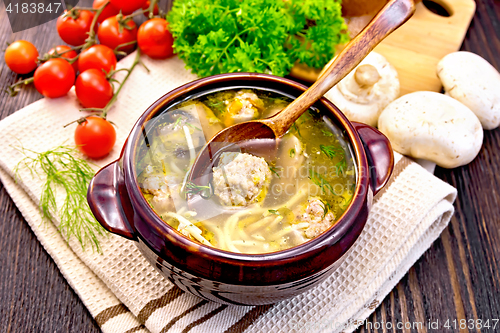 Image of Soup with meatballs and spoon in clay bowl on napkin