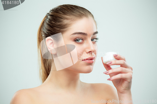 Image of Portrait of young beautiful woman applying moisturizing cream on her face