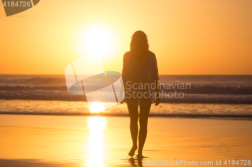 Image of Lady walking on sandy beach in sunset.