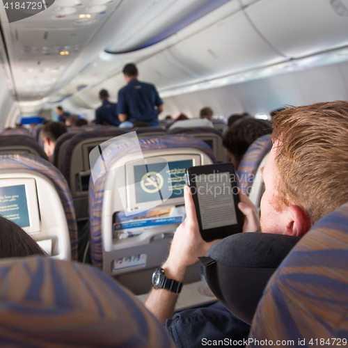 Image of Male passenger reading e-book on electronic reader on airplane.