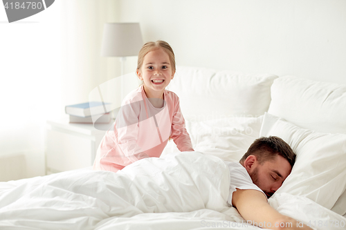 Image of little girl waking her sleeping father up in bed