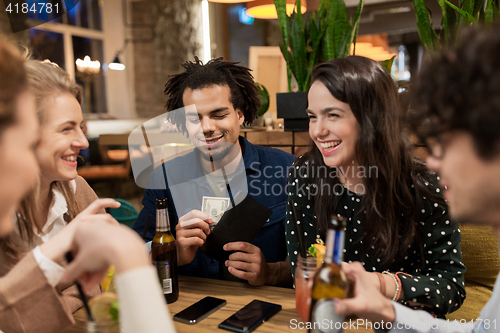 Image of friends with drinks, money and bill at bar