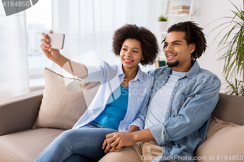 Image of happy couple with smartphone taking selfie at home