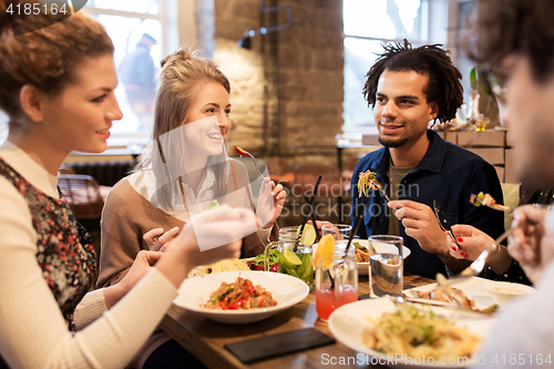 Image of happy friends eating and drinking at restaurant