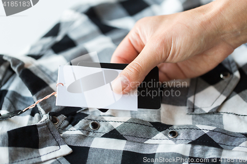 Image of close up of hand holding checkered shirt price tag