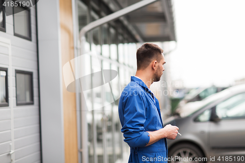 Image of auto mechanic smoking cigarette at car workshop