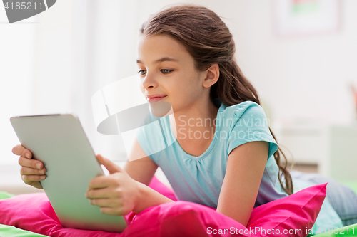 Image of smiling girl with tablet pc lying in bed at home