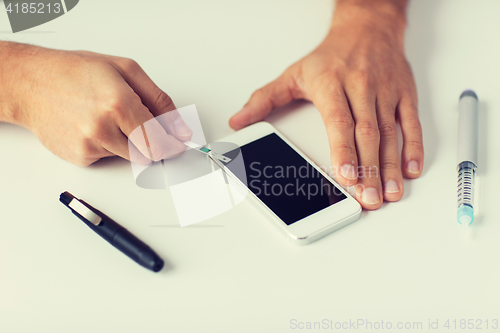 Image of close up of man with smartphone making blood test