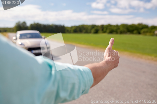 Image of man hitchhiking and stopping car with thumbs up