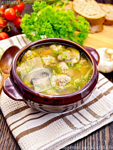 Image of Soup with meatballs and mushrooms in brown bowl on board