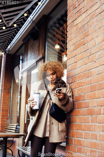 Image of young pretty african american women drinking coffee outside in c