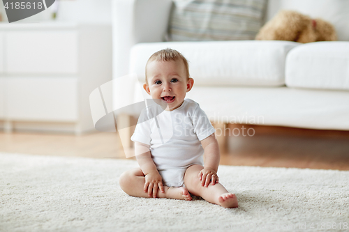 Image of happy baby boy or girl sitting on floor at home