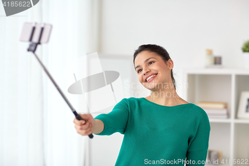 Image of woman taking selfie by smartphone monopod at home