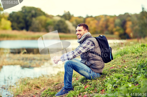 Image of smiling man with backpack resting on river bank