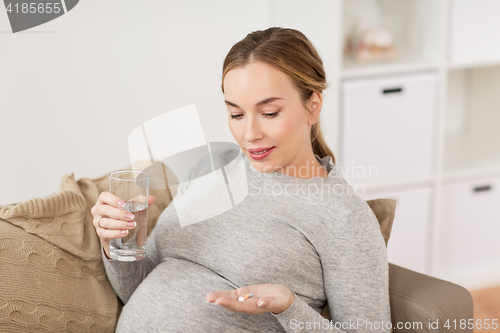 Image of happy pregnant woman with water and pills at home