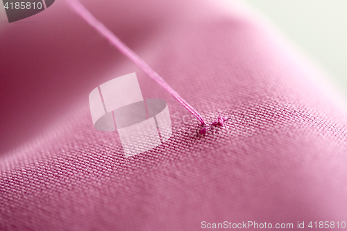 Image of thread with cross-stitch on pink fabric