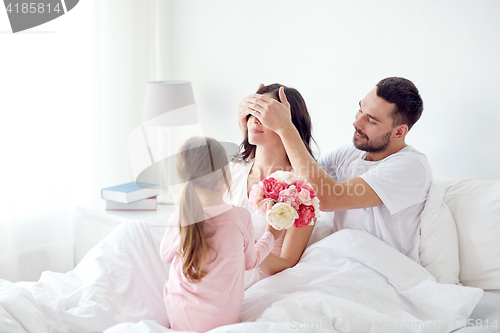 Image of happy girl giving flowers to mother in bed at home