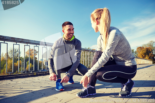 Image of smiling couple tying shoelaces outdoors