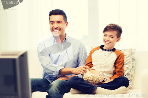 Image of smiling father and son watching tv at home