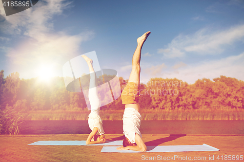 Image of couple making yoga headstand on mat outdoors