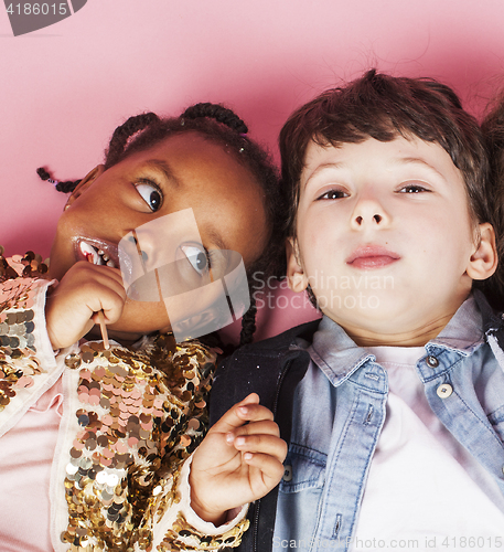 Image of little cute caucasian boy and african american girl hugging playing on pink background, happy smiling diverse nation and age children, lifestyle people concept close up