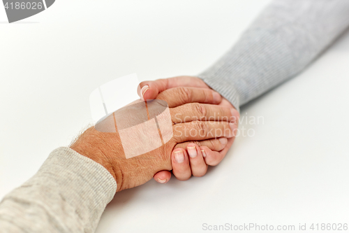 Image of close up of old man and young woman holding hands