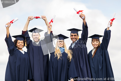 Image of happy students in mortar boards waving diplomas