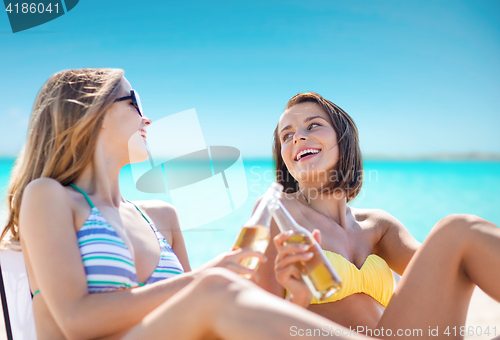 Image of happy young women with drinks sunbathing on beach