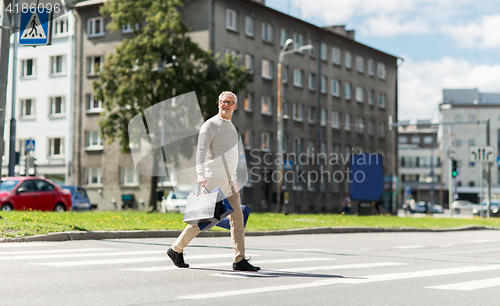 Image of senior man with shopping bags walking on crosswalk