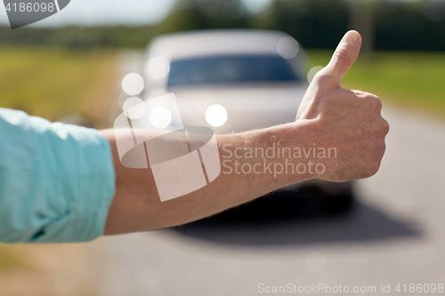 Image of man hitchhiking and stopping car with thumbs up