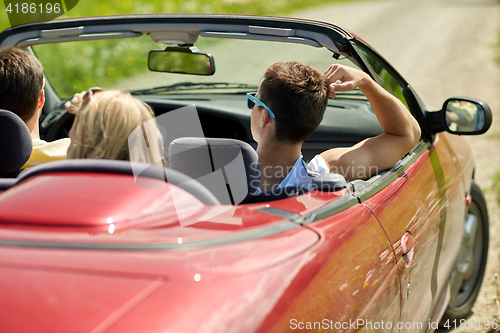 Image of happy friends driving in convertible car at summer