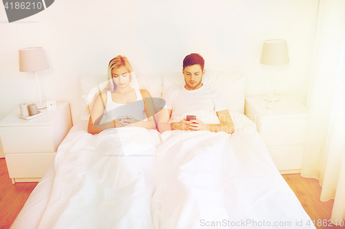 Image of couple with smartphones in bed