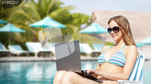 Image of happy young woman in shades with laptop on beach