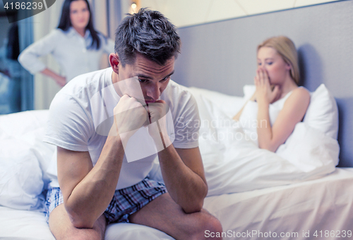 Image of man sitting on the bed with two women on the back