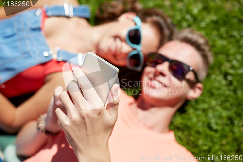 Image of happy teenage couple smartphone lying on grass