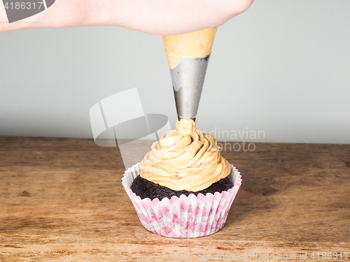 Image of Professional cake baker applying frosting onto a chocolate cupca