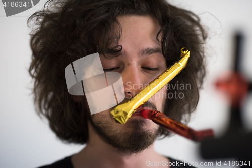 Image of Portrait of a man in party hat blowing in whistle